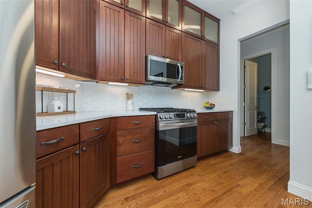 1804 Sterling Oaks Dr, Saint Peters, MO 63376 - kitchen with stainless steel appliances, light countertops, light wood finished floors, backsplash, and glass insert cabinets