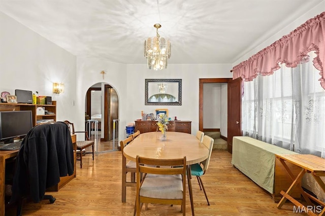 dining area with arched walkways, a chandelier, and light wood-type flooring