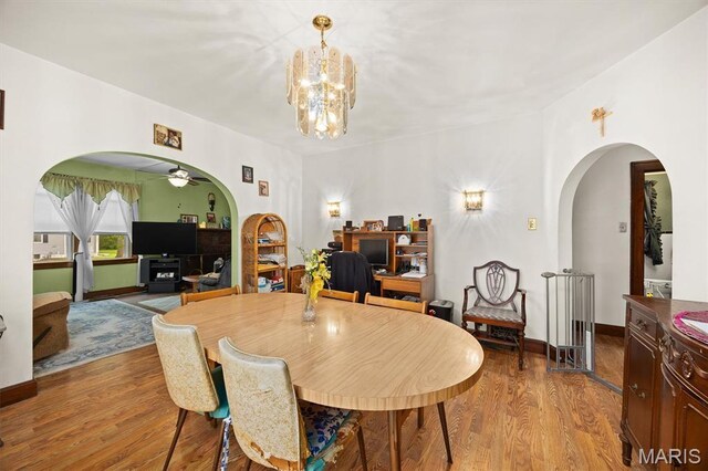dining space with arched walkways, wood finished floors, a chandelier, and ceiling fan