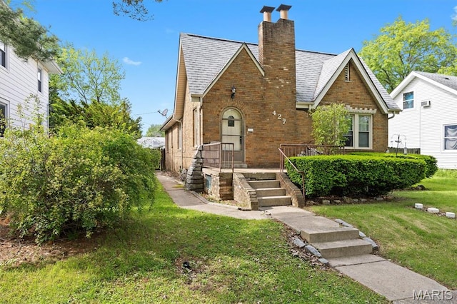 tudor home featuring brick siding, a front lawn, and a chimney