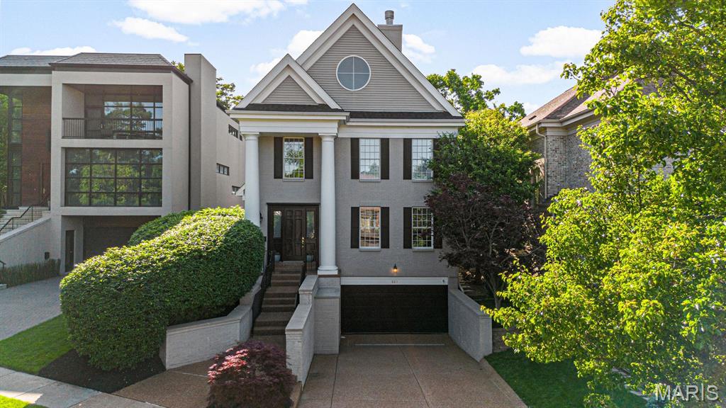 greek revival house featuring a garage, driveway, stucco siding, and a chimney