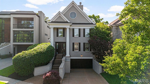 greek revival house featuring a garage, driveway, stucco siding, and a chimney