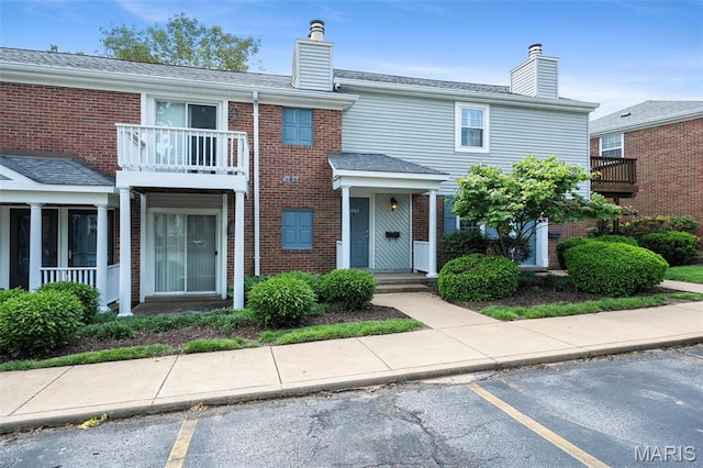 townhome / multi-family property featuring a chimney, brick siding, a balcony, and uncovered parking