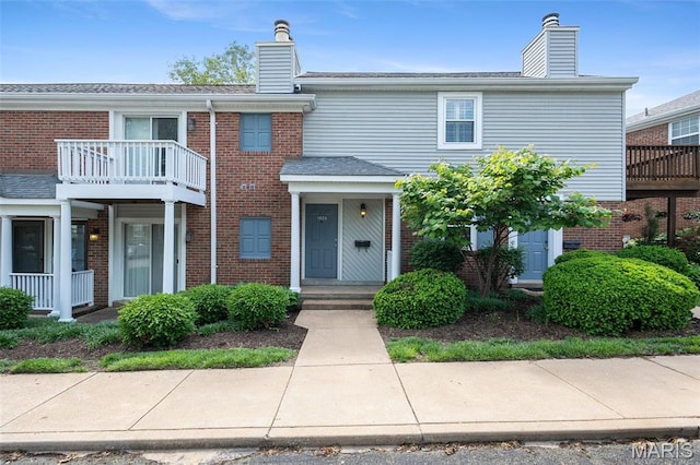 townhome / multi-family property with a chimney, brick siding, and a balcony