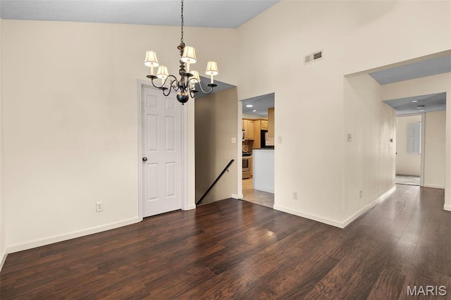spare room with a chandelier, dark wood finished floors, baseboards, and a high ceiling