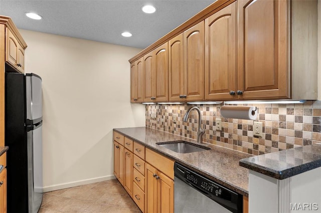 kitchen with appliances with stainless steel finishes, a sink, baseboards, backsplash, and dark stone countertops