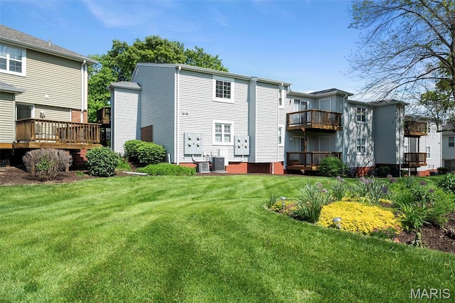 back of property featuring a lawn, central air condition unit, a balcony, and a wooden deck