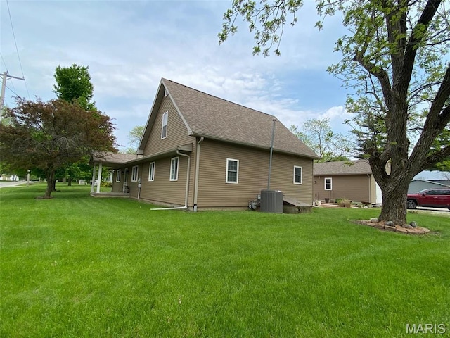 view of side of property featuring a yard, central AC, and a shingled roof