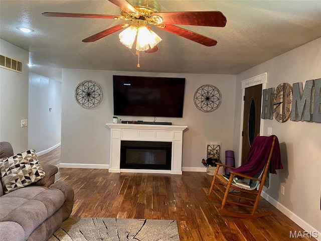 living area featuring a textured ceiling, wood finished floors, ceiling fan, baseboards, and a glass covered fireplace