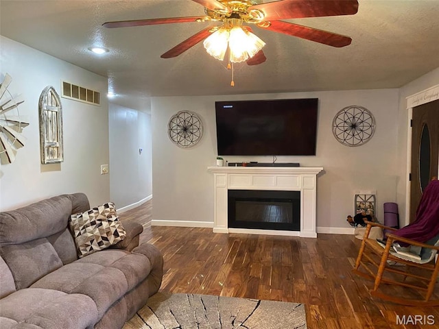living area with a ceiling fan, dark wood-style flooring, baseboards, and a textured ceiling