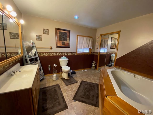 bathroom featuring toilet, a garden tub, vanity, a wainscoted wall, and tile patterned floors