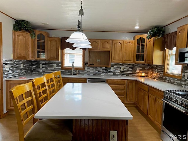kitchen featuring a sink, stainless steel appliances, decorative backsplash, light countertops, and ornamental molding