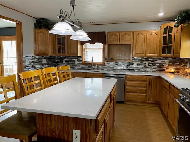 kitchen featuring appliances with stainless steel finishes, brown cabinets, glass insert cabinets, a sink, and ornamental molding