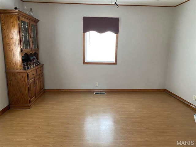 empty room featuring light wood-type flooring, baseboards, and ornamental molding