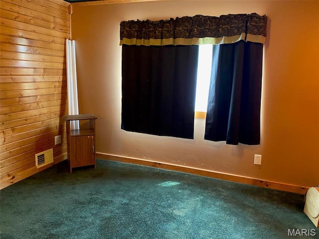 spare room featuring carpet floors, wooden walls, and baseboards