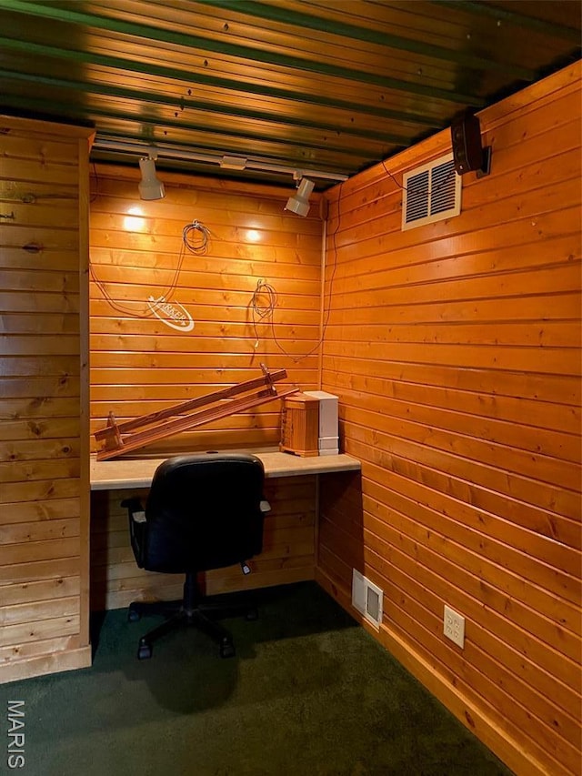 office area featuring wood walls, dark carpet, and built in desk