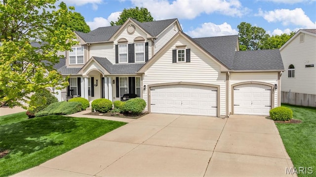traditional-style house with a front yard, driveway, a shingled roof, and a garage