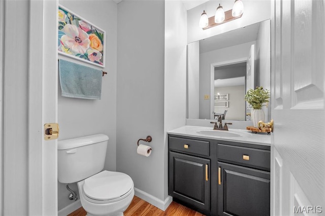 bathroom featuring baseboards, toilet, wood finished floors, and vanity