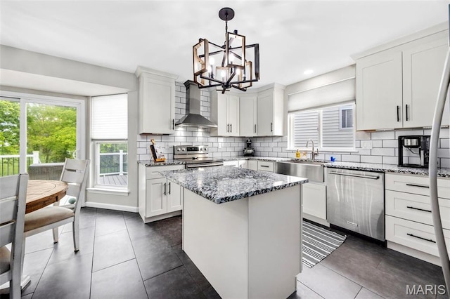 kitchen with wall chimney range hood, stainless steel appliances, a sink, a chandelier, and a kitchen island