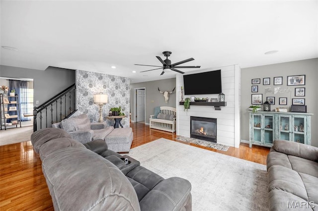 living area featuring stairs, ceiling fan, a fireplace, wood finished floors, and baseboards