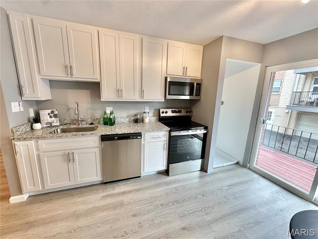 kitchen with appliances with stainless steel finishes, a sink, light wood finished floors, light stone counters, and white cabinetry
