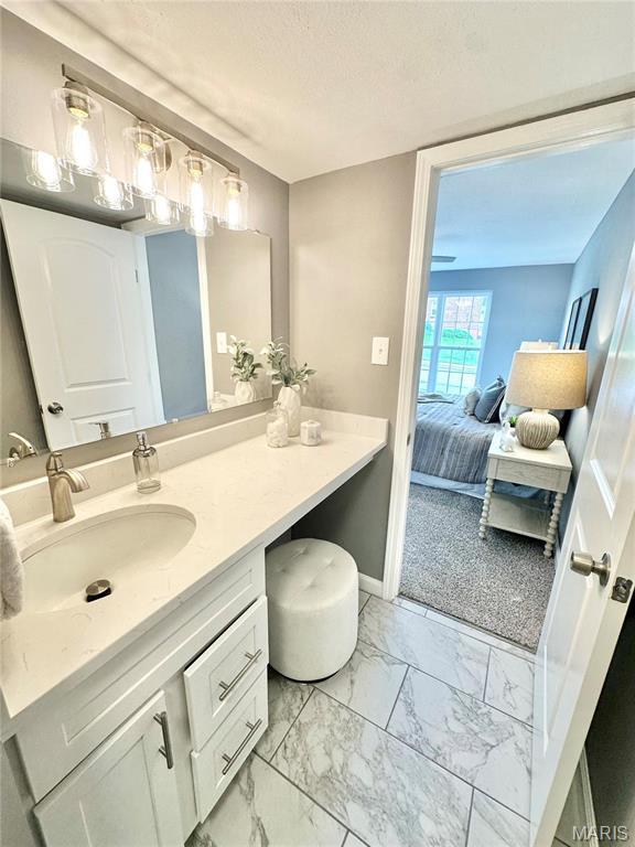ensuite bathroom with marble look tile flooring, vanity, baseboards, and a textured ceiling