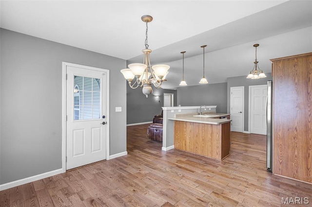 kitchen with a chandelier, a sink, light wood finished floors, baseboards, and light countertops
