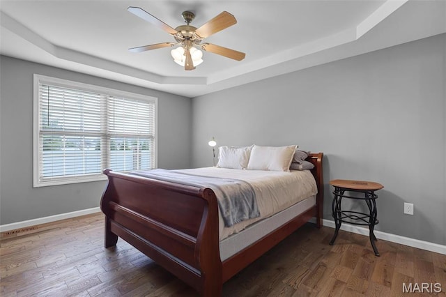 bedroom featuring a tray ceiling, baseboards, wood finished floors, and ceiling fan