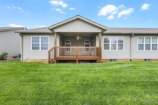 rear view of property with ceiling fan, a yard, a deck, and roof with shingles