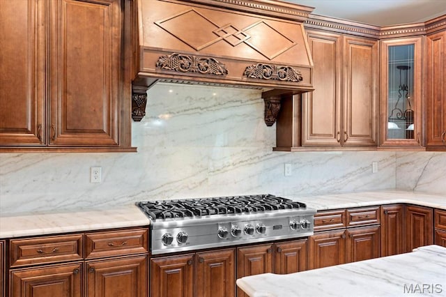 kitchen with custom range hood, stainless steel gas cooktop, tasteful backsplash, and glass insert cabinets