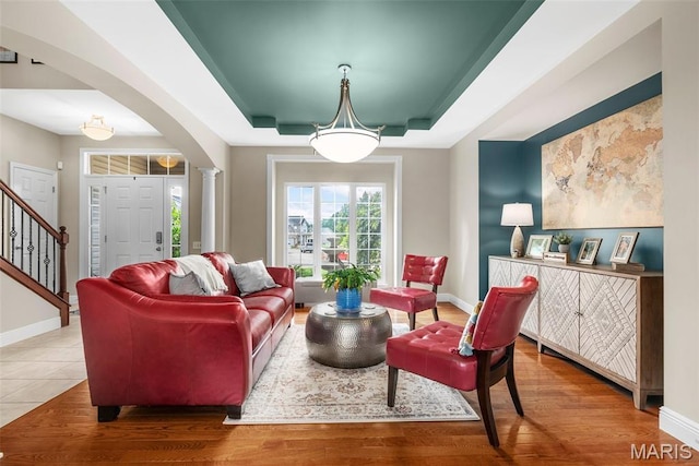 living area featuring arched walkways, baseboards, a raised ceiling, and wood finished floors