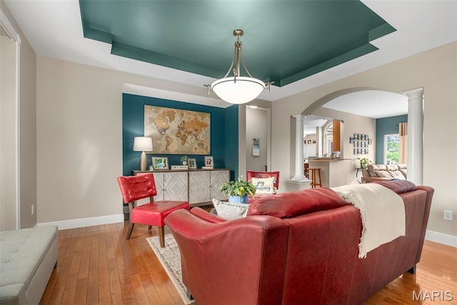 living area with ornate columns, a tray ceiling, arched walkways, and wood-type flooring