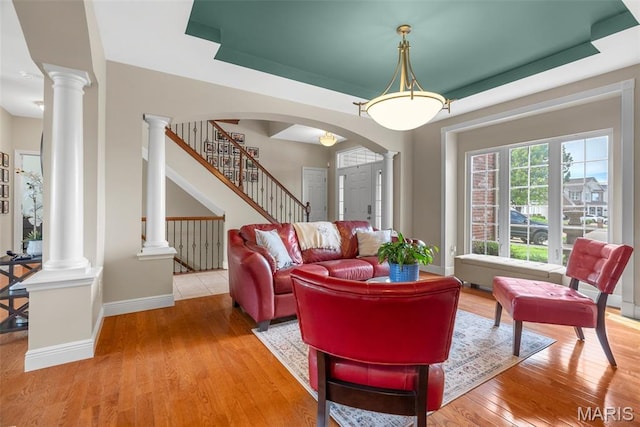 living area featuring ornate columns, wood finished floors, baseboards, arched walkways, and stairs