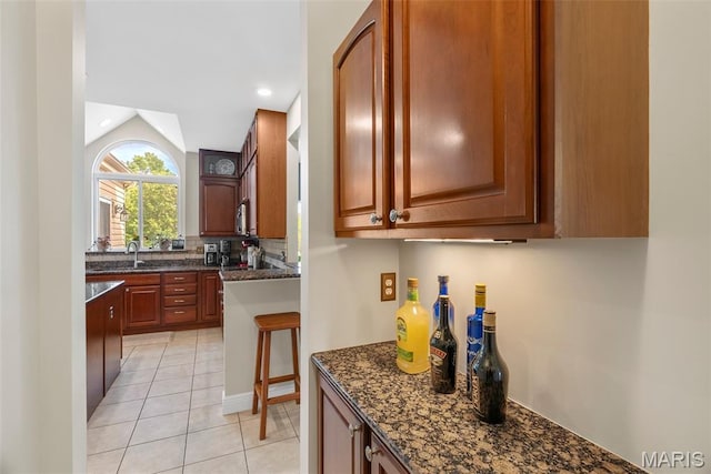 kitchen with light tile patterned flooring, dark stone counters, backsplash, lofted ceiling, and a sink