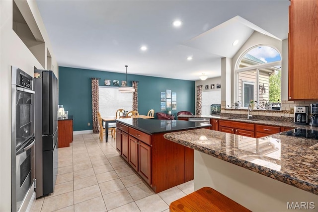 kitchen with brown cabinetry, a sink, light tile patterned floors, dark stone countertops, and decorative backsplash