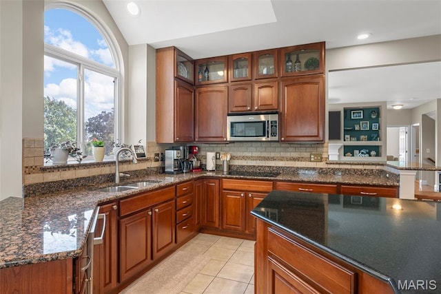 kitchen featuring stainless steel microwave, a sink, tasteful backsplash, dark stone counters, and vaulted ceiling