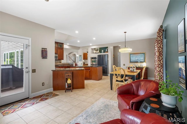 kitchen with brown cabinets, appliances with stainless steel finishes, light tile patterned floors, dark countertops, and arched walkways