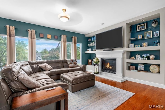 living area featuring wood finished floors, built in features, a glass covered fireplace, and baseboards