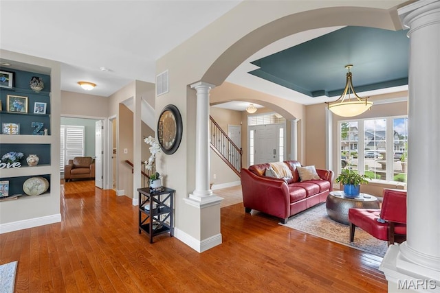 living area with decorative columns, arched walkways, wood finished floors, baseboards, and stairway
