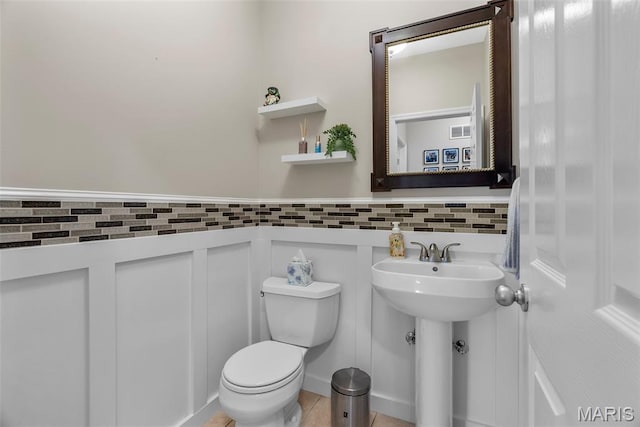 half bath with toilet, wainscoting, and a sink