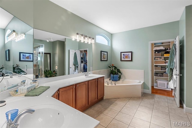 full bathroom with double vanity, a bath, a walk in closet, tile patterned floors, and baseboards