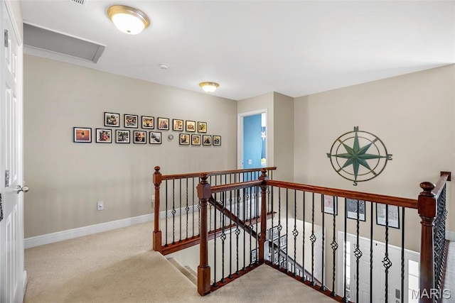 hall featuring an upstairs landing, attic access, baseboards, and carpet flooring