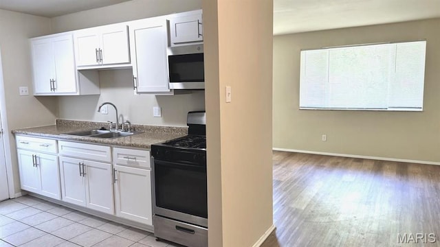 4028 Esseldale Dr, Saint Ann, MO 63074 - kitchen with stainless steel appliances, a sink, white cabinets, light wood-style flooring, and baseboards