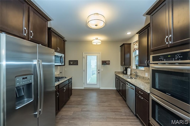 17006 Main St, Wildwood, MO 63040 - kitchen featuring appliances with stainless steel finishes, dark brown cabinets, light stone countertops, a sink, and baseboards