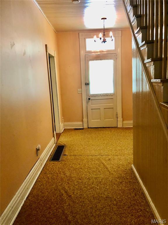 doorway to outside with a chandelier, baseboards, light colored carpet, and stairs
