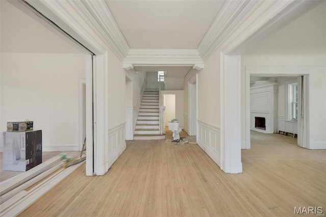 hallway with a decorative wall, crown molding, stairway, light wood finished floors, and a wainscoted wall