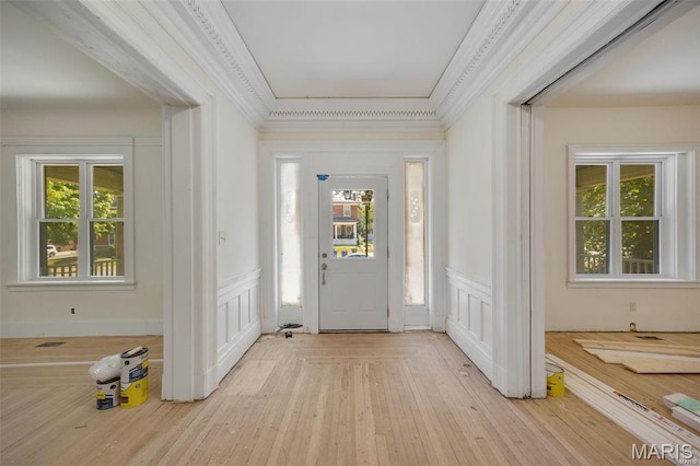 foyer entrance featuring a decorative wall, wainscoting, crown molding, and light wood-type flooring