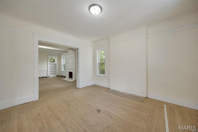 empty room with baseboards, a fireplace with flush hearth, and wood finished floors