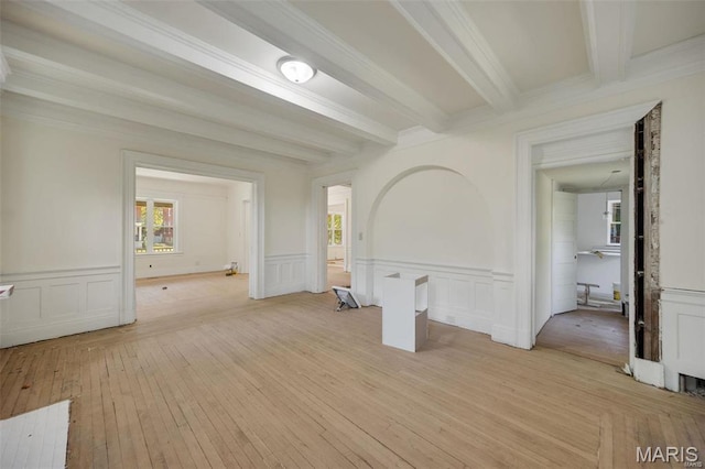 unfurnished living room featuring beam ceiling, light wood-type flooring, ornamental molding, and a decorative wall