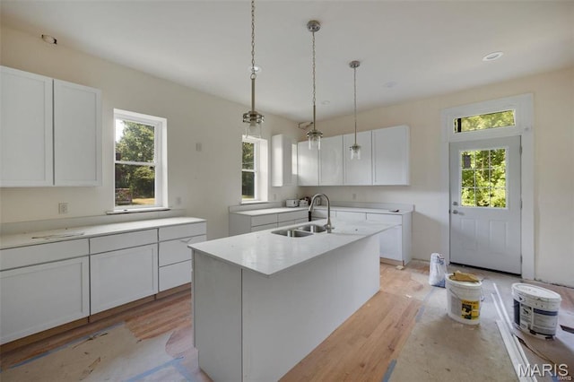 kitchen with a sink, light wood finished floors, hanging light fixtures, white cabinetry, and recessed lighting